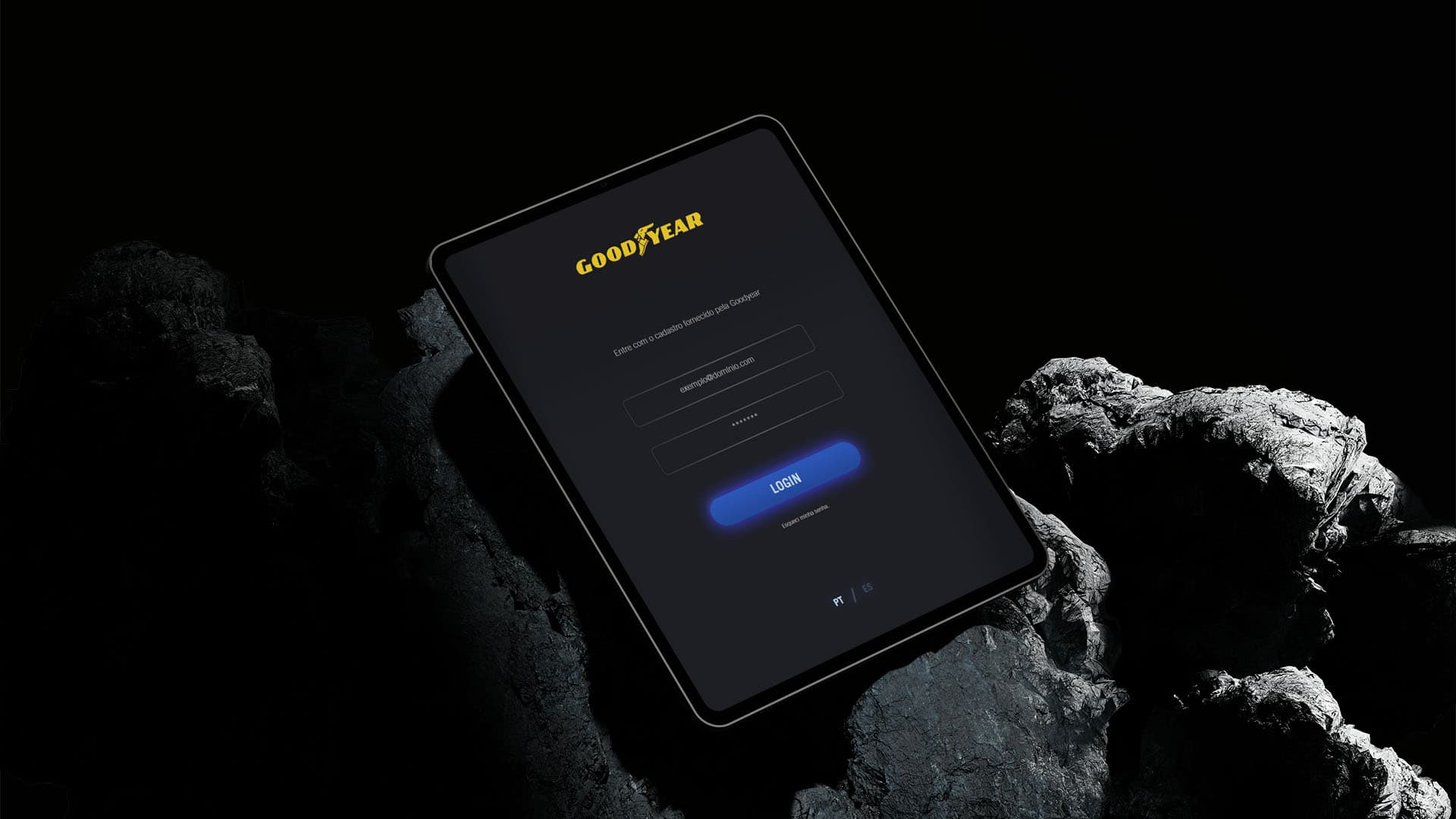 Tablet exibindo a tela de login do aplicativo da Goodyear com opções de idioma em português e espanhol, apoiado sobre uma pedra
